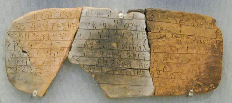 An ancient, fragmented clay tablet in three reassembled pieces, featuring rows of inscribed Linear B script.