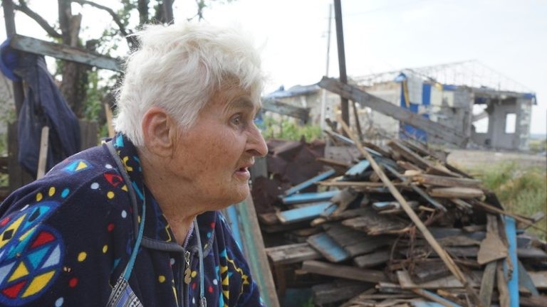 A Ukrainian woman stands in the wreckage of her home