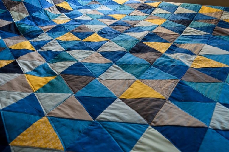 A close-up view of a patchwork quilt stitched together in a geometric pattern of blue, yellow, and grey triangles.