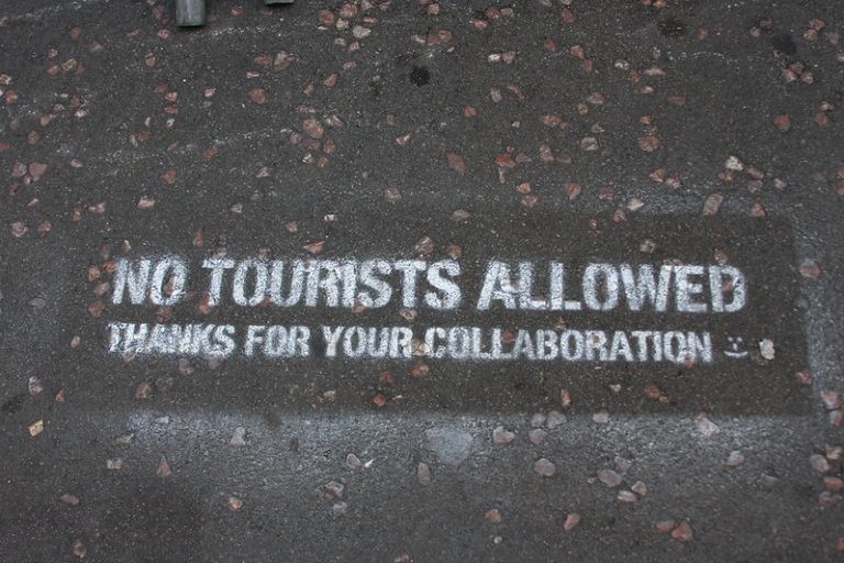 Painted text on a street saying "No tourists allowed. Thanks for your collaboration".