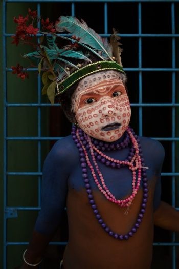 Person with face paint, beads, and feather head piece.