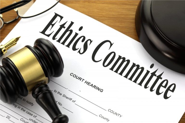 A gavel and eyeglasses rest on a legal document titled "Ethics Committee Court Hearing."