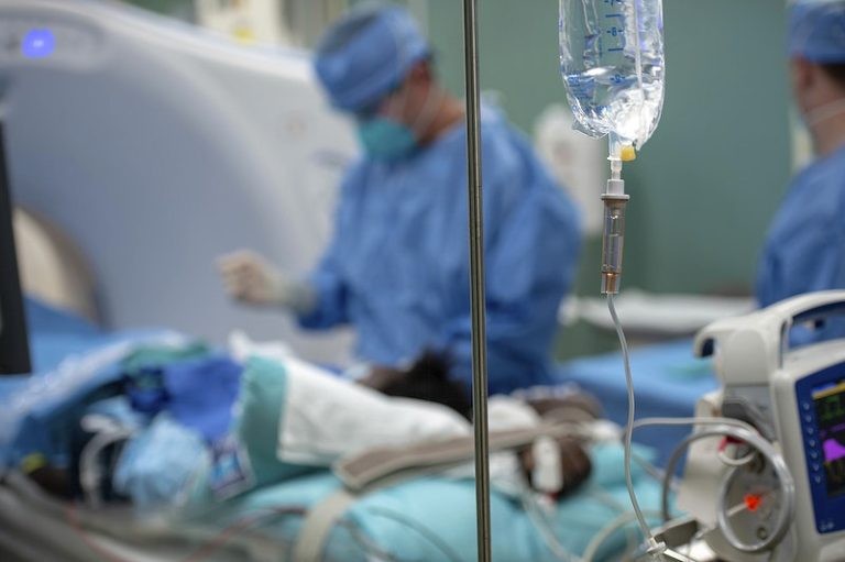 Intravenous drip line in the foreground with medical staff preparing a patient for a scan in an operating room