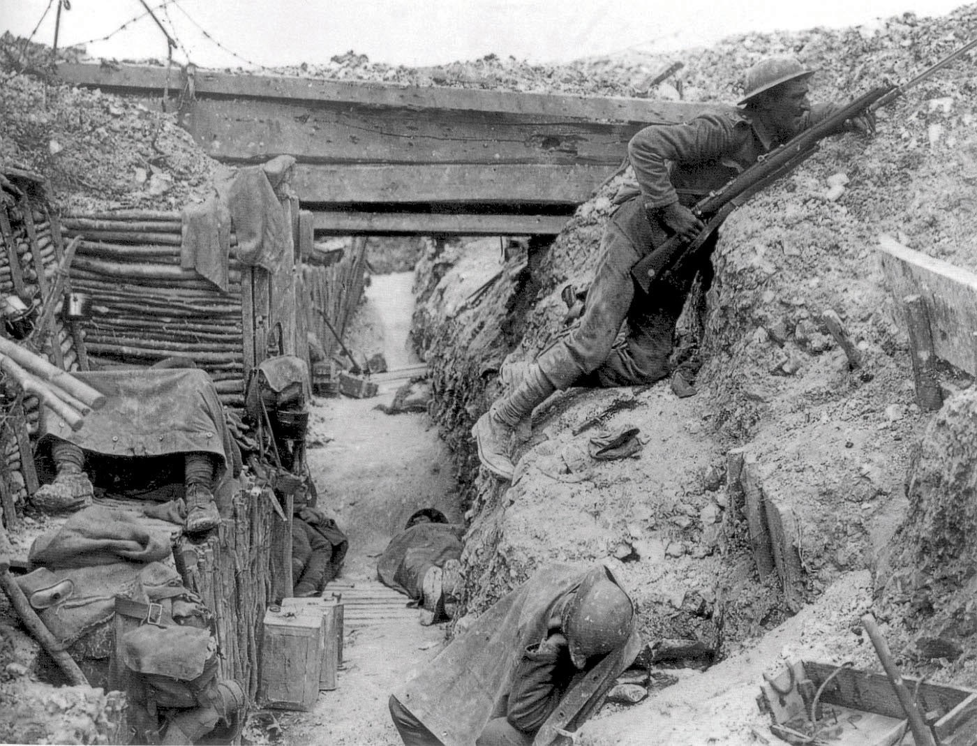 Black and white photo of a WWI trench. Wooden supports, barbed wire, and soldiers. Some look injured or dead.