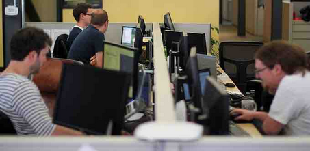 Office scene with multiple people working at computers. Some looking at screens, others typing. 