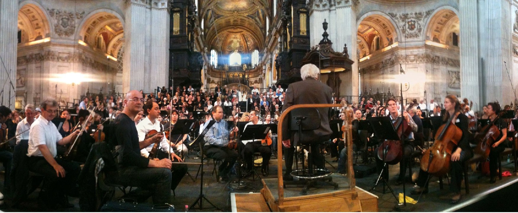 The conductor is in a dark suit facing the orchestra from behind. Orchestra in foreground and choir in the distance
