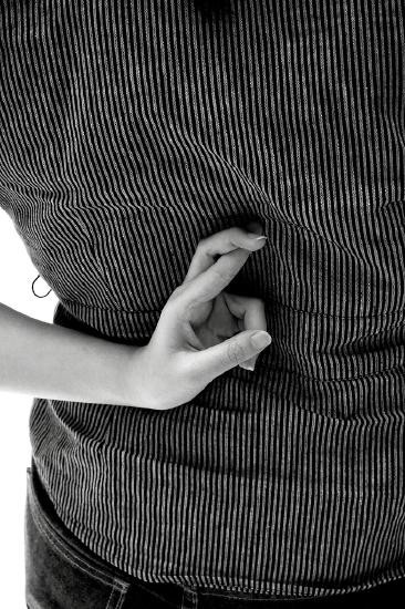 Black and white photo of a person crossing their fingers behind their back over a striped shirt.