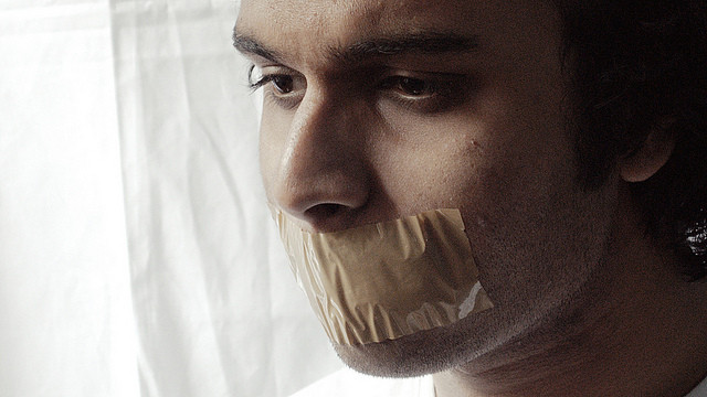 Close-up profile view of a man with thick tan tape covering his mouth.