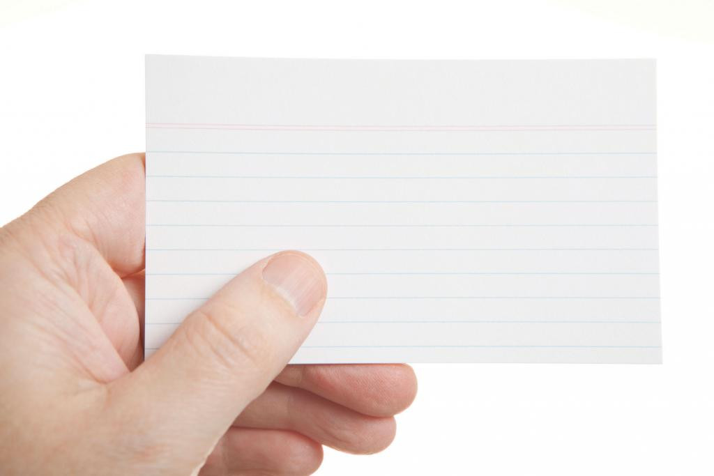 A close-up view of a hand holding a blank, white-lined index card against a plain white background.