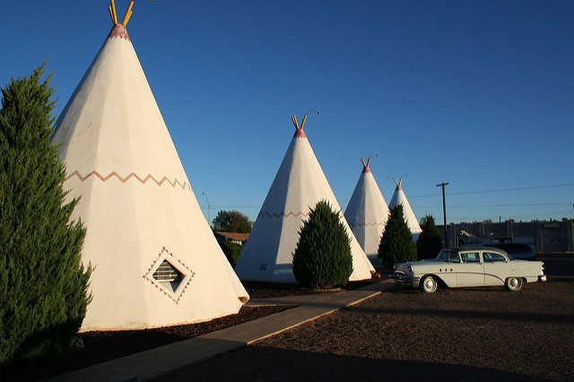 A row of white concrete teepee cabins at a vintage roadside motel with a classic white car parked outside.